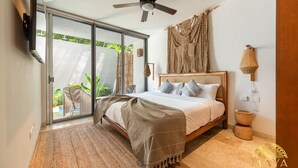 A bedroom with a bed, a ceiling fan, a large sliding glass door leading to a balcony, and a woven wall hanging. - NHOA 102A Lux 2BR Condo Plunge Pool in Aldea Zama (Tulum)