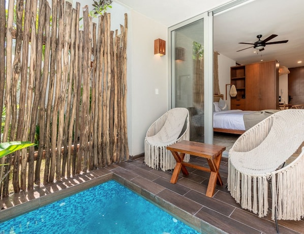Une chambre moderne dotée d’une porte vitrée donnant sur une chambre à coucher, d’un petit espace piscine avec deux chaises et d’un ventilateur de plafond.