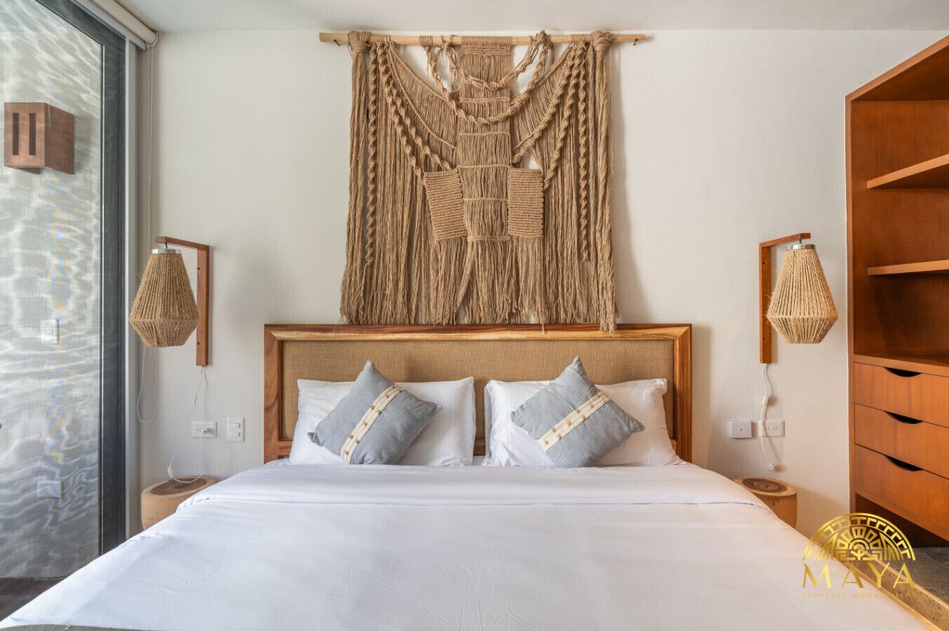Una habitación de hotel con una cama grande, cabecera de madera y un colgador de macramé en la pared.