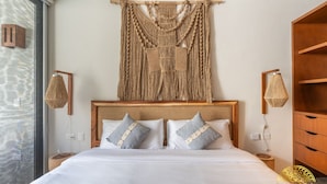 A hotel room with a large bed, wooden headboard, and a macrame wall hanging.