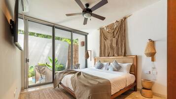 Un dormitorio con cama, ventilador de techo, ventana grande y vista a zonas verdes.