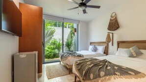 A bedroom with a bed, a ceiling fan, a TV, a refrigerator, and a view of greenery outside.