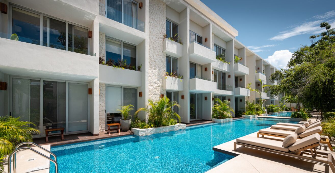 A modern hotel with a large pool, outdoor seating, and balconies with plants.