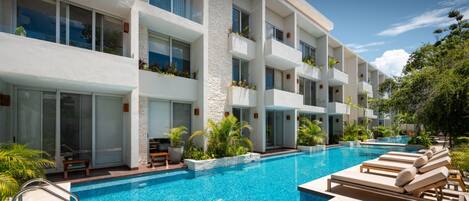 A modern hotel with a large pool, outdoor seating, and balconies with plants.