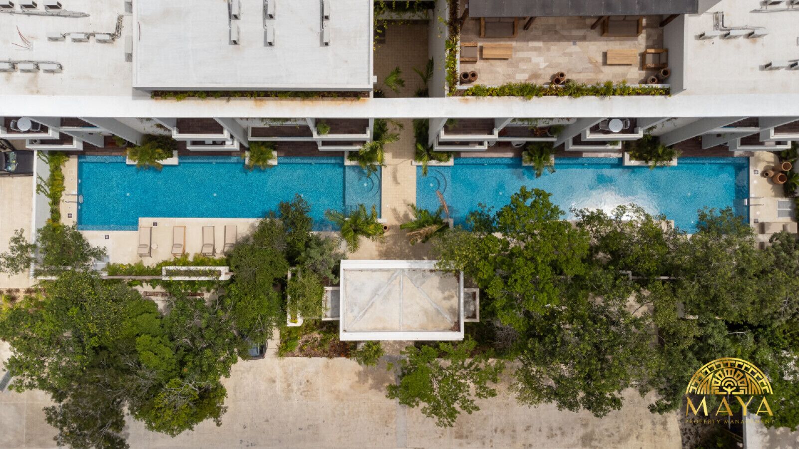 A high-rise building with two swimming pools, surrounded by trees and greenery.