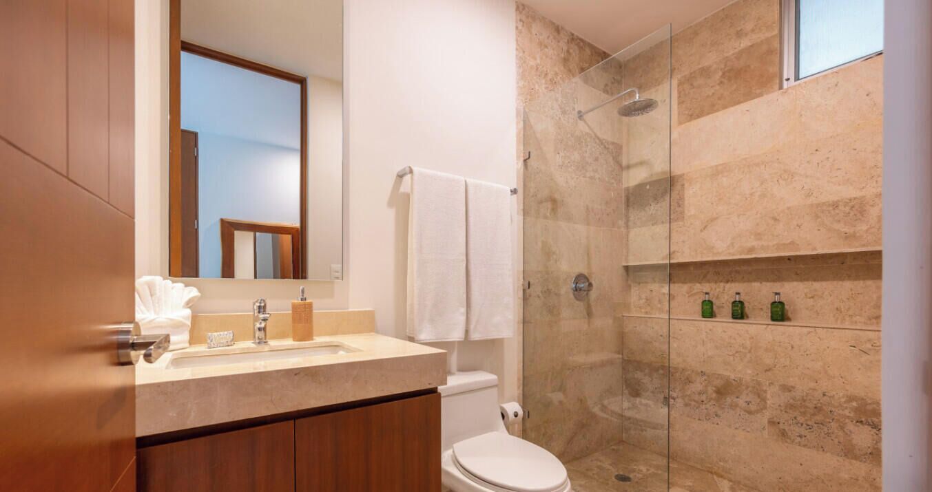 A modern bathroom with a marble shower, a toilet, and a vanity with a mirror and sink.