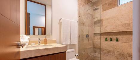 Un baño moderno con ducha de mármol, inodoro y tocador con espejo y lavabo.