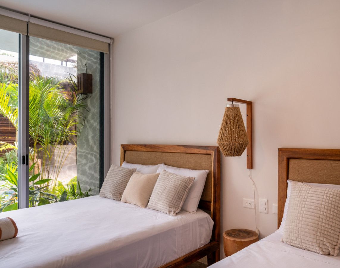 Une chambre d’hôtel avec deux lits, une grande fenêtre et une vue sur la verdure environnante.