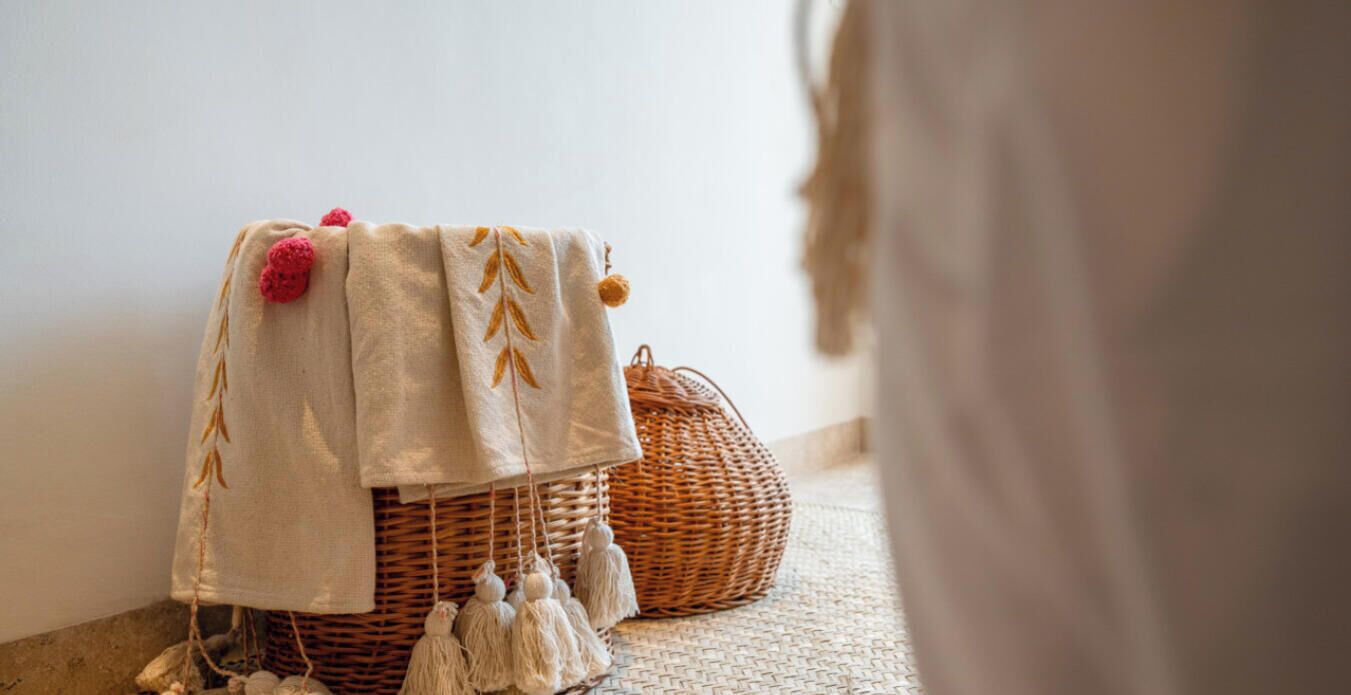 A wicker basket with a cloth cover and tassels on a woven floor.
