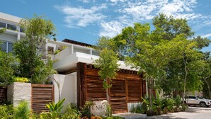 A modern building with a white facade, wooden shutters, and a stone base. - NHOA 302C Lux 1BR Condo Top Jungle View Aldea Zama (Tulum)