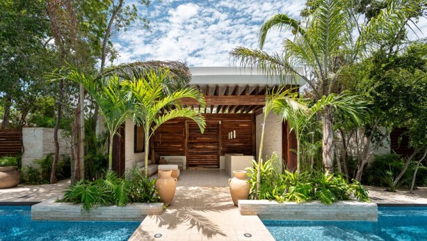 A poolside area with a wooden pergola, palm trees, and a stone wall. - NHOA 302C Lux 1BR Condo Top Jungle View Aldea Zama (Tulum)