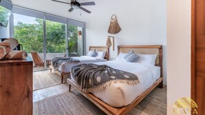 Un dormitorio con dos camas, un ventilador de techo y un ventanal con vistas a árboles.