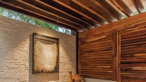 Area esterna con sedute, parete in pietra, soffitto in legno e un pannello decorativo in tessuto.