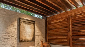 An outdoor seating area with a stone wall, wooden beams, and a woven wall hanging. - NHOA 311C Lux 1BR Condo Pool View in Aldea Zama (Tulum)