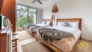 A modern bedroom with two beds, a ceiling fan, a large window, and a view of greenery. - NHOA 311C Lux 1BR Condo Pool View in Aldea Zama (Tulum)