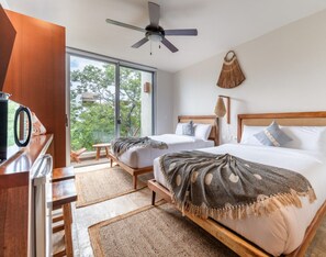 Een moderne slaapkamer met twee bedden, een plafondventilator, een groot raam en uitzicht op groen.