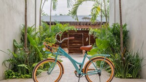 A turquoise bicycle with orange wheels parked in a lush garden area with tall plants and a wooden fence in the background. - NHOA 101B Lux 1BR Condo Pool access in Aldea Zama (Tulum)