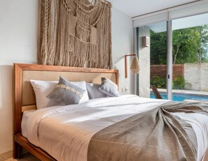 Een slaapkamer met een groot bed, een macramé wanddecoratie, en uitzicht op een zwembad en groen buiten.