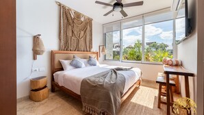 Ein Schlafzimmer mit einem Bett, einem Deckenventilator, einem Fernseher, einem Fenster mit Blick und einem kleinen Tisch.