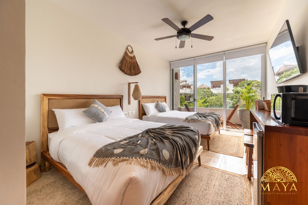A hotel room with two beds, a ceiling fan, a large window with a view, and a television on a wooden cabinet.