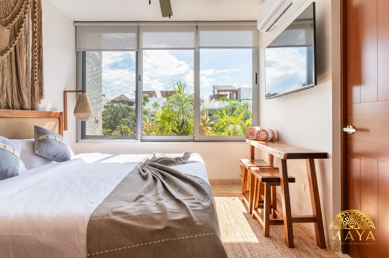 A bedroom with a large window, a bed, a desk, and a chair.