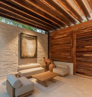 An outdoor seating area with a stone wall, wooden ceiling, and a woven wall hanging. - NHOA 305A Lux 2BR Condo Pool View in Aldea Zama (Tulum)