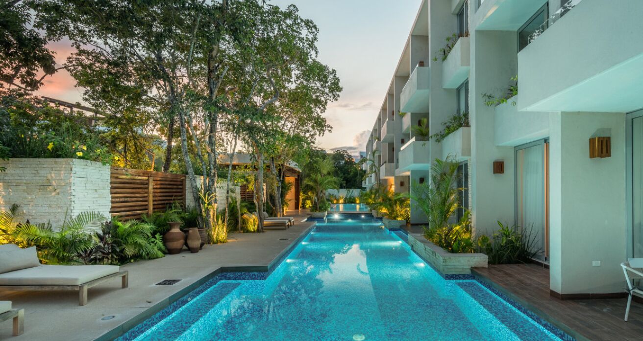 A swimming pool with a view of a modern building, surrounded by greenery and outdoor seating.