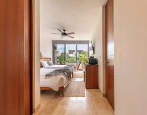 A hotel room with a bed, a ceiling fan, a TV, and a view of the outdoors.