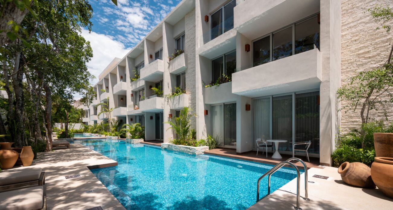 A modern hotel with a swimming pool, outdoor seating, and balconies with plants.