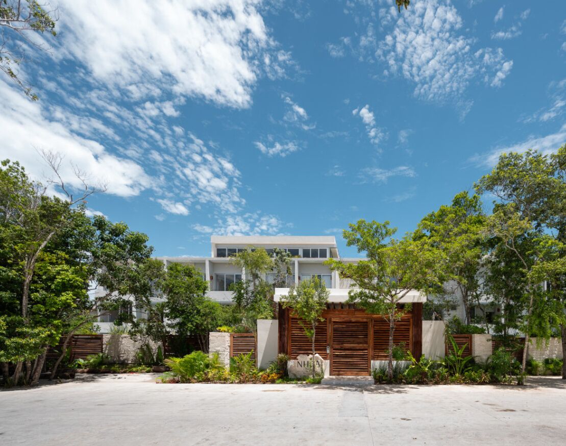 A modern house with a spacious front yard, a large wooden gate, and a clear blue sky.