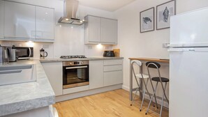A modern kitchen with white cabinetry, a built-in oven, a gas stove, and a white refrigerator. There are two bar stools and a wooden countertop. - 2 bedroom accommodation in Nairn (Nairn)