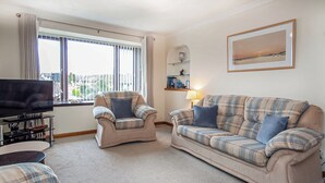 A living room with a sofa, armchair, and television. - 2 bedroom accommodation in Nairn (Nairn)