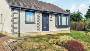 A two-story house with a tiled roof, stone facade, and a front yard with various plants. - 2 bedroom accommodation in Nairn (Nairn)