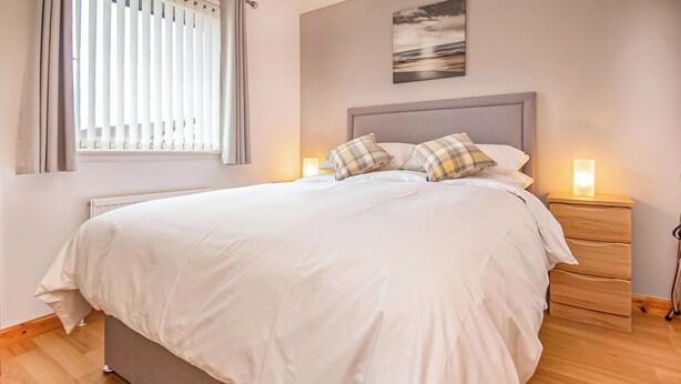 A neatly made bed with white bedding, a grey headboard, and two bedside tables with lamps. - 2 bedroom accommodation in Nairn (Nairn)