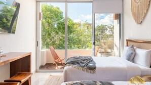 A bedroom with a large sliding glass door leading to a balcony, a bed with a blanket, a wooden desk, and a chair.