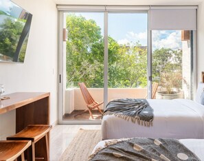 A bedroom with a large sliding glass door leading to a balcony, a bed with a blanket, a wooden desk, and a chair.