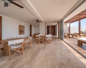A spacious dining area with wooden tables and benches, large windows offering a view of the outdoors, and a ceiling fan.