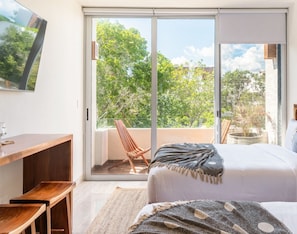 A bedroom with a large sliding glass door leading to a balcony, a bed with a blanket, a wooden desk, and a chair.