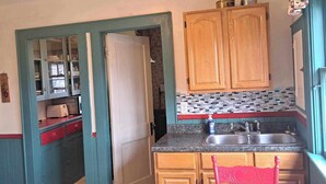 A compact kitchen with wooden cabinets, a sink, and a red chair. - Downtown heritage flat near everything (Dartmouth)