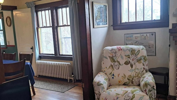 A room with a floral armchair, a radiator, a window with curtains, and a framed picture on the wall. - Downtown heritage flat near everything (Dartmouth)