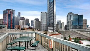 A rooftop terrace with a table and chairs, overlooking a cityscape with modern high-rise buildings. - 2BR, 2BA Cozy, Central, Downtown Convention Center (Seattle)