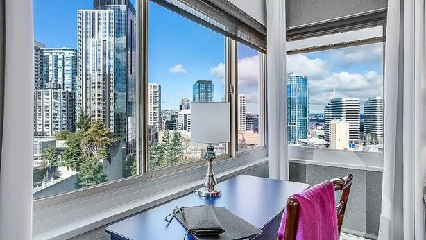 A room with a desk, chair, and a view of tall buildings through large windows. - 2BR, 2BA Cozy, Central, Downtown Convention Center (Seattle)