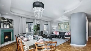 A modern living room with a dining area, featuring a fireplace, a chandelier, and a large window with curtains. - 2BR, 2BA Cozy, Central, Downtown Convention Center (Seattle)