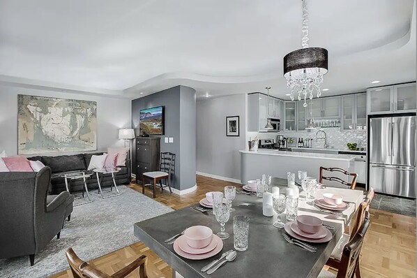 A modern living room with a grey sofa, a dining table set for six, and a kitchen with stainless steel appliances. - 2BR, 2BA Cozy, Central, Downtown Convention Center (Seattle)