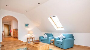 A spacious loft apartment with a high ceiling, a skylight, and a cozy seating area with two blue sofas. - 2 bedroom accommodation in Dornoch (Dornoch)