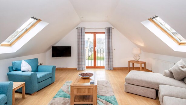 A spacious loft apartment with a high ceiling, skylights, a large sliding glass door leading to a balcony, and a modern interior with a blue sofa, beige sofa, and a wooden coffee table. - 2 bedroom accommodation in Dornoch (Dornoch)
