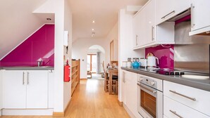 A modern kitchen with white cabinets, a stainless steel range hood, and wooden flooring. - 2 bedroom accommodation in Dornoch (Dornoch)