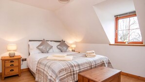 A bedroom with a bed, two bedside tables, a nightstand, a wooden bench, a window, and a ceiling light fixture. - 2 bedroom accommodation in Dornoch (Dornoch)