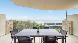 Un patio con una mesa y sillas, una planta en maceta y vistas a la playa y al océano.