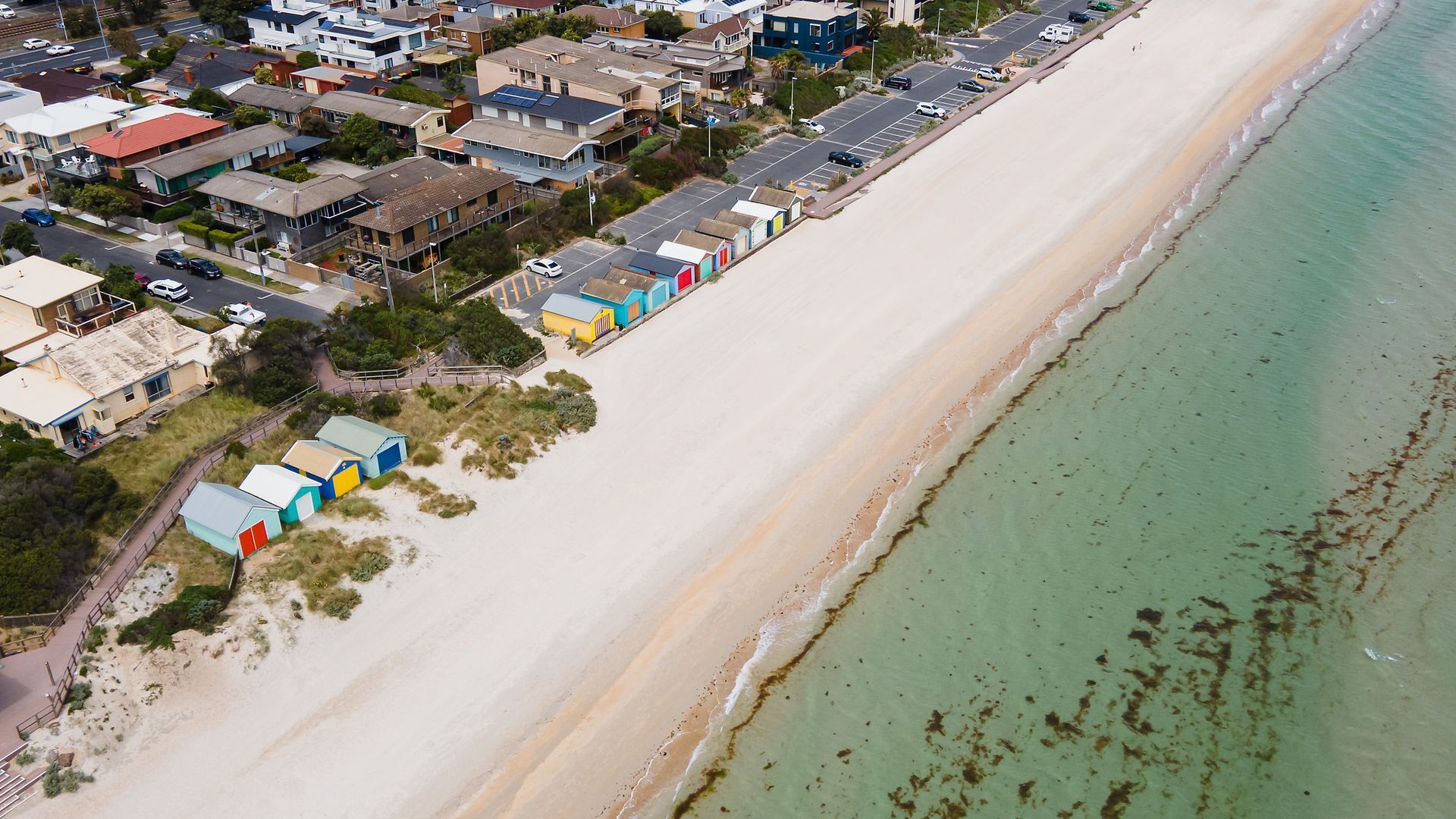 Luftaufnahme einer Küstenlandschaft mit Strand, Häusern und bunten Strandhäusern.